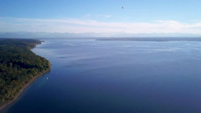 Aerial drone cinematic hot air ballon  fly over Lake Starnberg Munich Germany Europe at Schloss Seeburg Castle with stunning scenic Bavarian Alps autumn deep blues water forward slowly pan up movement