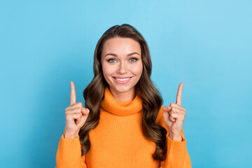 Photo of pretty sweet woman dressed orange sweater pointing two fingers up empty space isolated blue color background