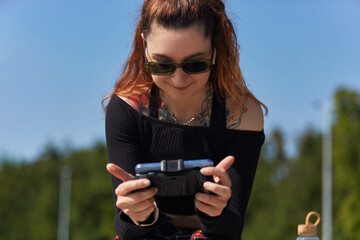 Cheerful gamer playing mobile game on a smart phone with a gamepad. Portrait of a tattooed young adult female in sunglasses gaming online with a modern gadget © hurricanehank
