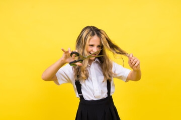 A young girl about to cut her own hair with a pair of scissors, isolated against yellow background