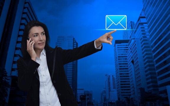 Businesswoman hand press email icon over modern office city tower and skyscraper, Business contact us online concept