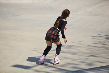 Young female skating in a outdoor skatepark in summer. Athletic person roller blading in a concrete...