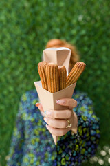 woman holding churros in cardboard box in front of green grass wall