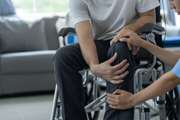 Fototapeta na wymiar Female physiotherapist working examining injured knee and leg of male patient in wheelchair, giving advice, treating pain in clinic, physiotherapy concept, health insurance.