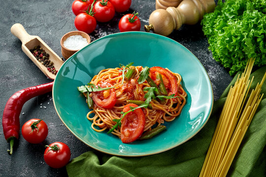 Pasta with tomatoes, asparagus and red sauce in a plate on a dark background.