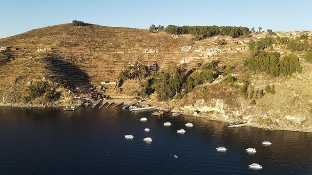 Aerial view of Isla del Sol at lake Titicaca in Bolivia, Drone view of paradise island hillsand small village with terraces on slopes and boats docked in hurbor