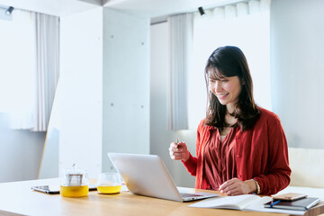 一人暮らしの部屋で大学や学校のオンライン授業をノートパソコンで受講する20代から30代の女性の学生