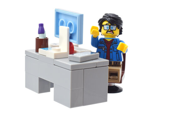 Lego minifigure toy  of awful pc user with angry face at slow computer isolated on white. Editorial illustrative image of popular plastic brick constructor.