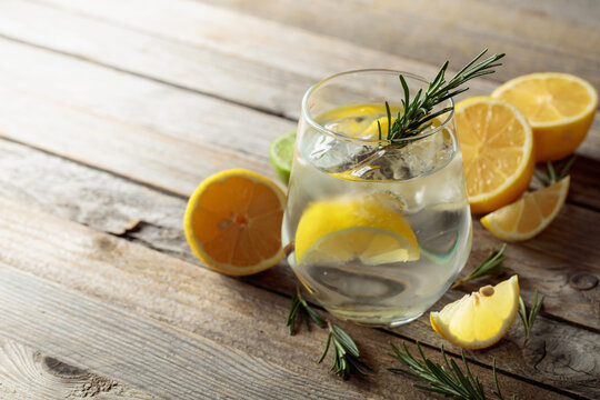 Gin tonic with ice, rosemary, and lemon slices on an old wooden table.