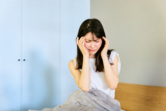 対人トラブルやハラスメントに巻き込まれ部屋の寝室で頭を抱えて悩む20代から30代の被害者の日本人女性