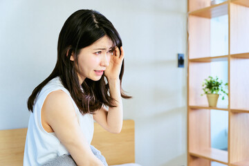 Fototapeta premium 寝起きの寝室で睡眠不足と体調不良で頭痛がして朝の光が眩しく感じる30代の1人暮らしの30代の女性