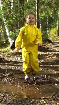 Little girl in a yellow rubber suit is jumping in a puddle.