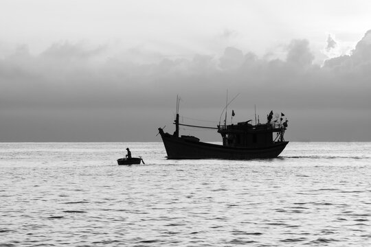 Black and white photo at sea with silhouettes of fishing boats and Vietnamese fishermen in the morning. The image has a high contrast of black and white.
