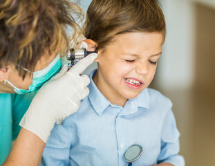 Little boy uncomfortable as he gets his ears checked by the doctor