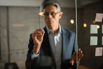 Portrait of successful businessman in office. Man writing on the glass board in office.