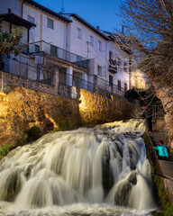 A waterfall lit up at night running through a town.