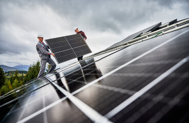 Workers building solar panel system on roof of house. Men technicians in helmets carrying...