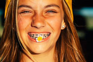 Portrait of beautiful blonde teen girl with a flower in her mouth and a bracket in her teeth.
