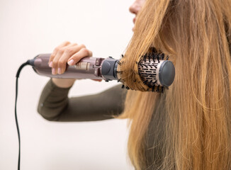 beautiful young woman using rotative brush hair styler for hair.female girl with long dark blonde...