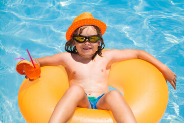 Kid floating in pool. Child relaxing in pool, drink summer cocktail. Outdoor summer activity for children. Happy child having fun at swimming pool on summer day. Kids summer cocktail in pool.