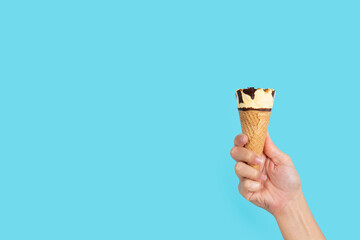 Hand holding ice cream cone on blue background. Copy space