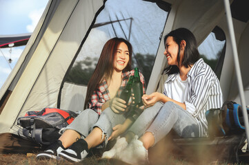 Asian couple women, LGBTQ teen couples travel sitting together drinks in camping tent evening time in a romantic nature atmosphere. LGBTQ lesbians, Lesbians girlfriend, Best friend.