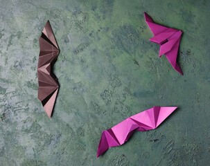 Purple and black paper origami bats on a green concrete background with space for text. DIY concept, children's art, creative. Halloween holiday.
