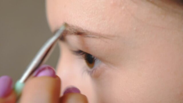Young brown eyed girl doing makeup with mascara. Attractive woman taking care of herself painting eyebrows. Beautiful model in beauty salon. Concept of fashion and style. Slow motion Detail view