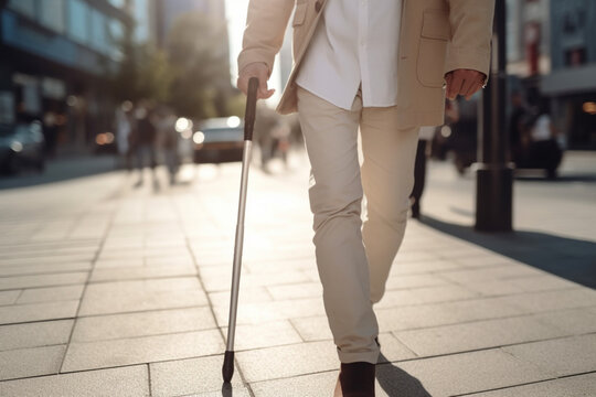 Midsection of young blind man with white cane walking across the street in city,