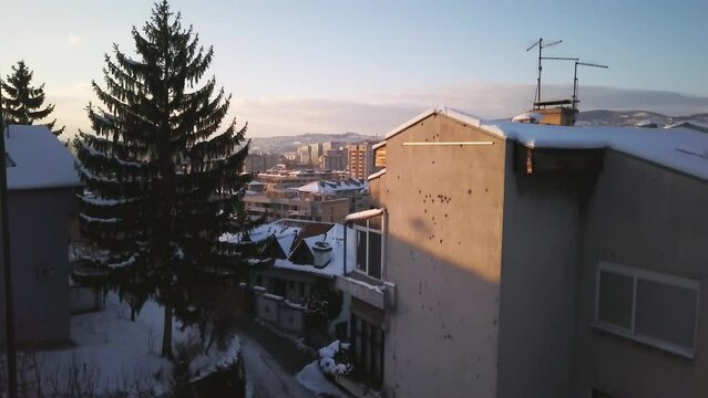 Aerial cinematic drone winter war zone bullet holes on building car driving Olympic downtown snowy frozen Sarajevo City town center Bosnia and Herzegovina frozen landscape sunset slow upward movement
