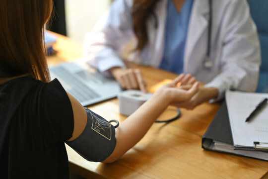 Cropped image of nurse measuring blood pressure female patient at table. Hypertension, medicine and healthcare concept