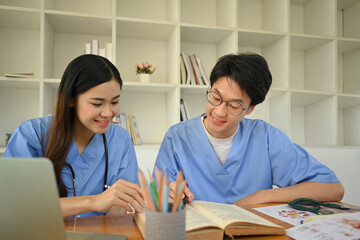 Two happy medical student reading books, preparing for university exams in library. Medical internship concept