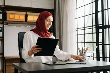 Young Arabic female entrepreneur wearing a hijab working online with a laptop at office