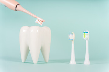 White healthy tooth model and a modern electric ultrasonic toothbrush with different toothbrush heads on blue background with copy space. Dental care and healthcare concept.