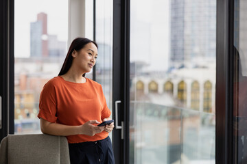 Young asian businesswoman in corporate office looking at view of city skyline