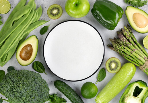 Healthy vegetarian food: green vegetables and herbs on a gray background. Top view. Copy space. Assorted green vegetables: broccoli, beans, avocado, zucchini, kiwi, asparagus. Alkaline diet. 