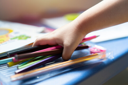 Cropped image of  a little child hand holding a colorful pencils, playing children using pencil crayons  at table indoors.