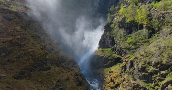 Spectacular misty western Norway waterfall flowing down steep lush canyon; drone