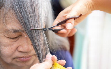 Working with hair scissors. Professional hairdresser woman cutting hair of mature woman. She is getting haircut at home.