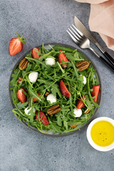 Salad with strawberries, mozzarella balls, arugula and pecans on gray background. Top view.