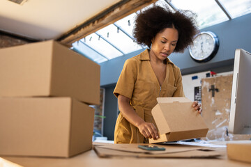 Female entrepreneur packing orders into cardboard boxes to ship