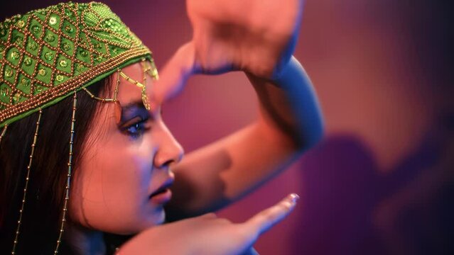 Indian woman belly dancer face in traditional headdress with jewelry rhinestone dancing at backlit