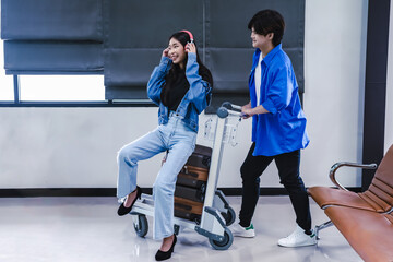 Traveller man pushing airport cart with woman sitting on luggage and listening music from heardphone, Airline Business
