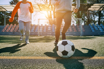 Father and Son play football on stadium, Happy family outdoors, bonding, family fun, players in soccer in dynamic action have fun playing football in sunny day, holidays time.
