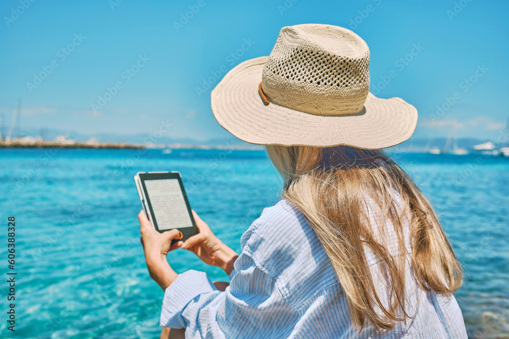 Wall mural fashion pretty woman outdoors lifestyle watching, reading on tablet ebook on the beach in summer day