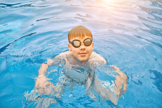 Smiling boy portrait in swimming goggles, Child swim in the pool, sunbathes, swimming in hot summer day. Relax, Travel, Holidays
