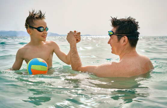 Happy family, father and son bonding, play ball, swim in the sea looking at view enjoying summer vacation. Togetherness Friendly concept
