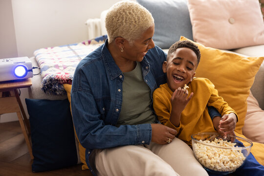 African American mother and son having watching a movie at home with popcorn