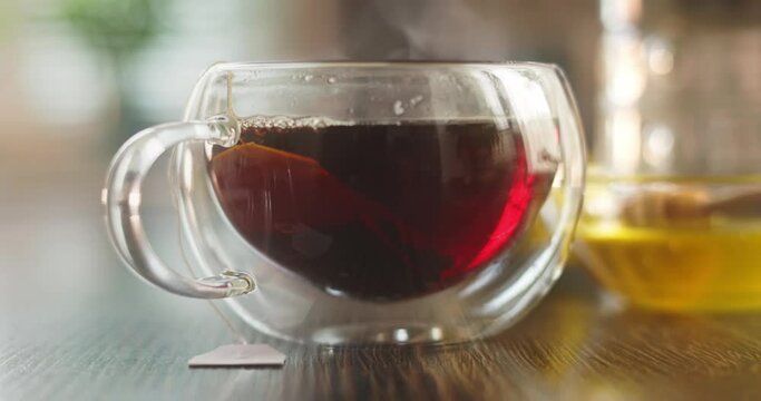 Steaming hot tea cup. Hot tea in glass cup with smoke on wooden table in kitchen