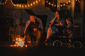 The family is resting in the evening near the campfire and their motorhome - obrazy, fototapety, plakaty